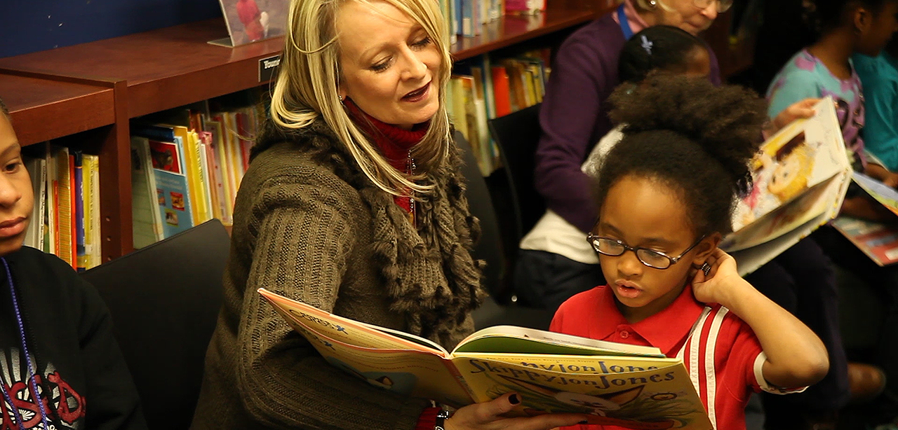 Woman helping young child read book