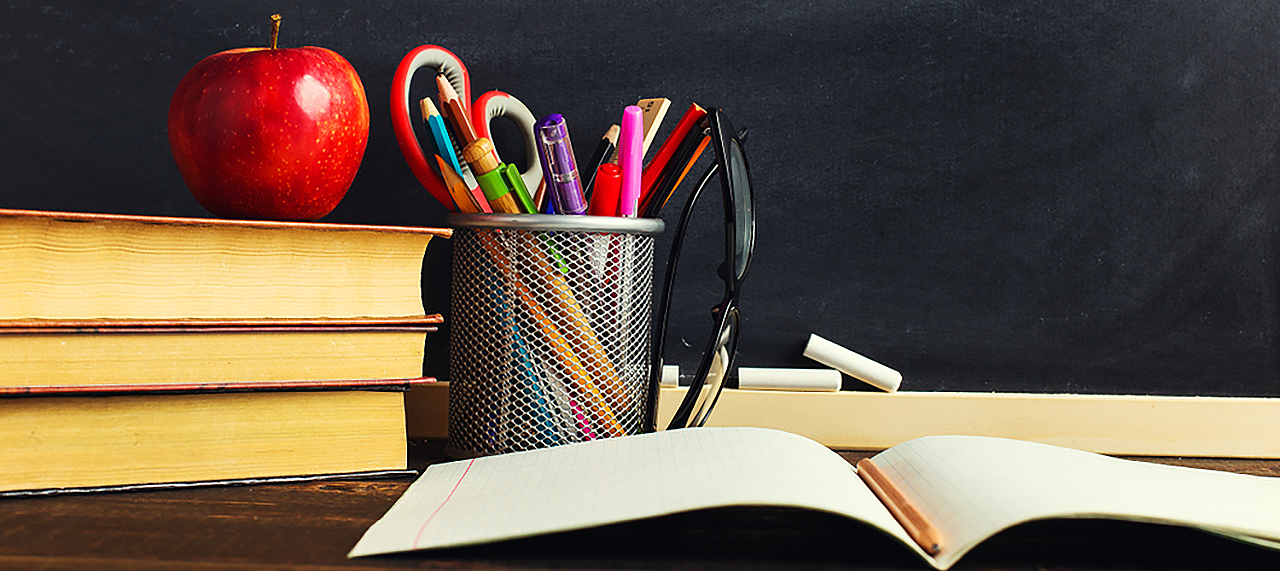 A teacher's desk with an open notebook, stack of books, and an apple