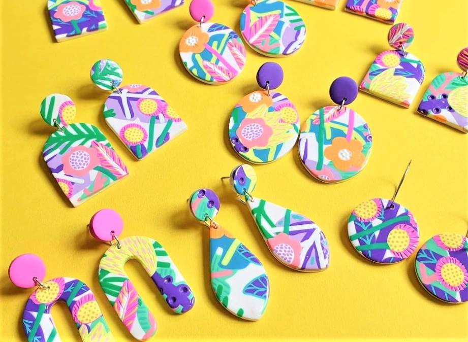 brightly colored polymer clay earrings in a variety of shapes with a floral-tropical design on a bright yellow background