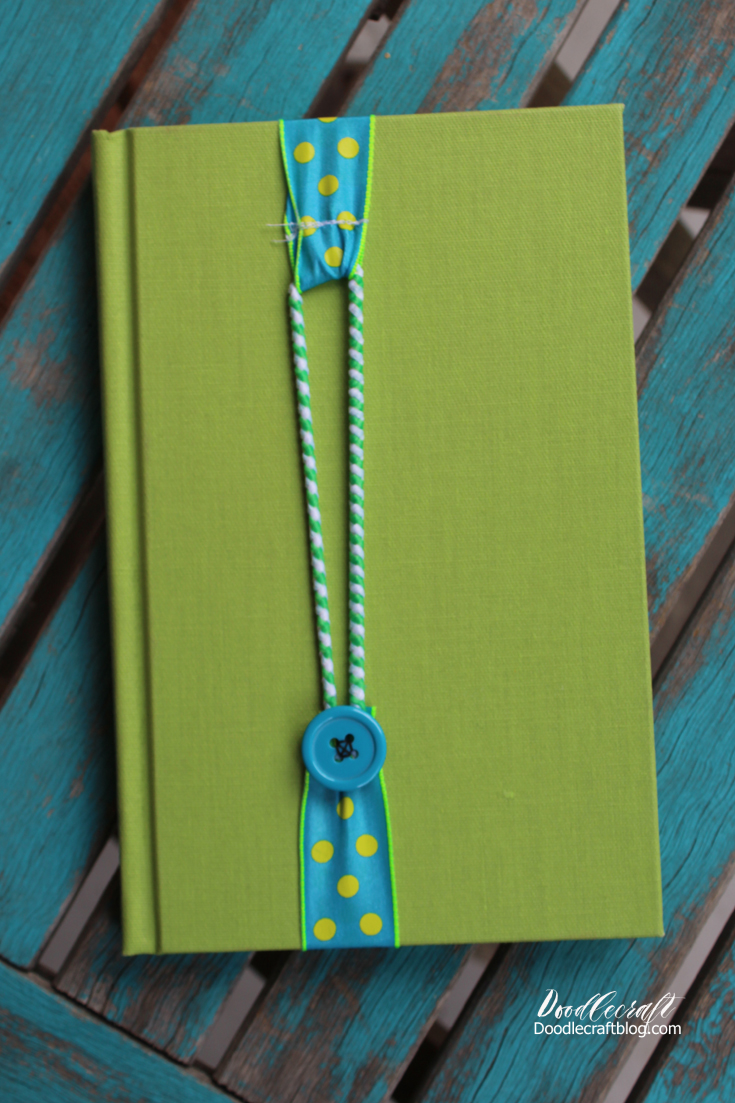 A book with a ribbon bookmark on it, held together by an elastic wrapped around a button.