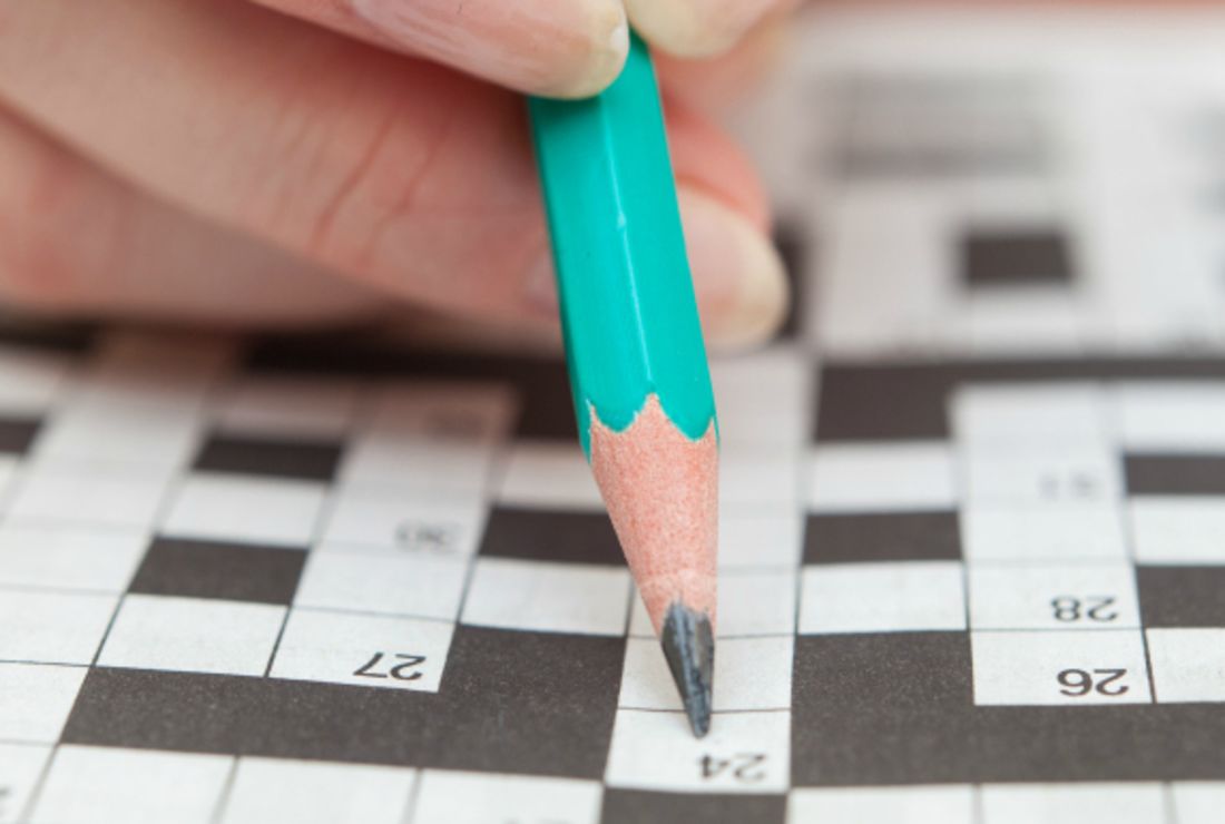 closeup of a person doing a crossword puzzle with a turquoise pencil