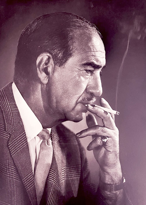 Photographic portrait of a man holding a smoking cigarette to his lips.