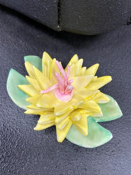 Clay sculpture of yellow flower with green leaves.