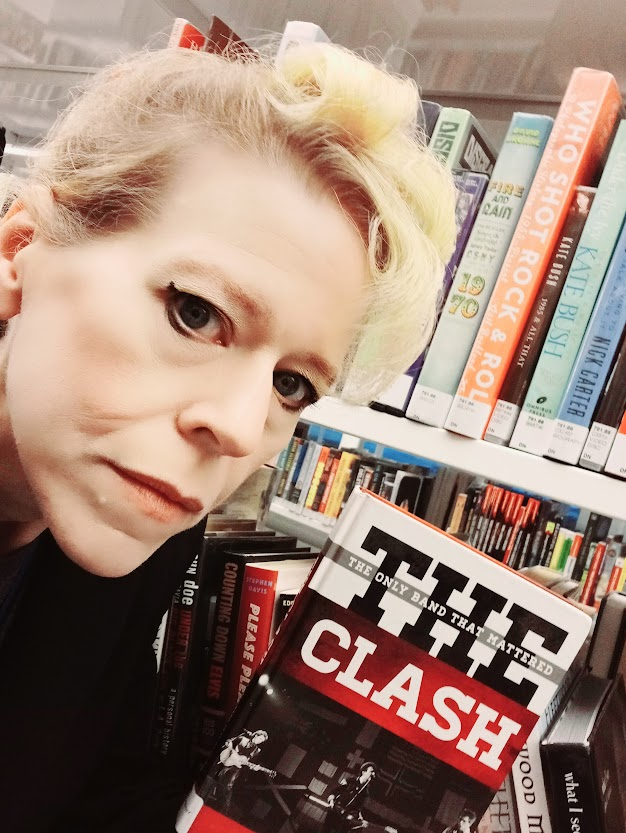 Granny Anarchy, a white femme with great eyeliner skills, holding up a copy of one of the books recommended in this essay.