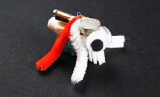 bristlebot made of a toothbrush head with a coin battery and pager motor on top and googly eyes, with red and white pipe cleaners for legs