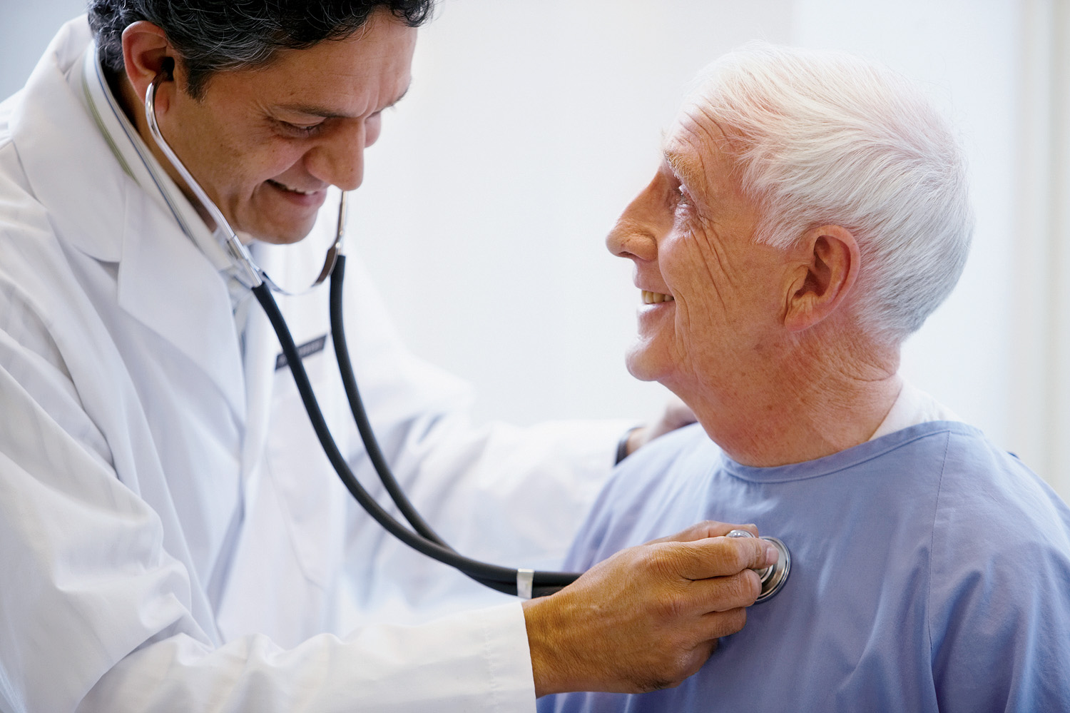 doctor holding stethoscope to older male patient's chest