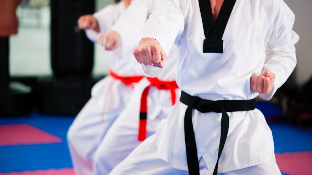 three taekwondo students; one black belt, two red belts