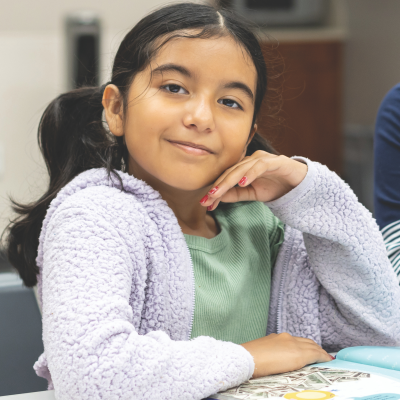 Young girl smiling at camera with book on a table.