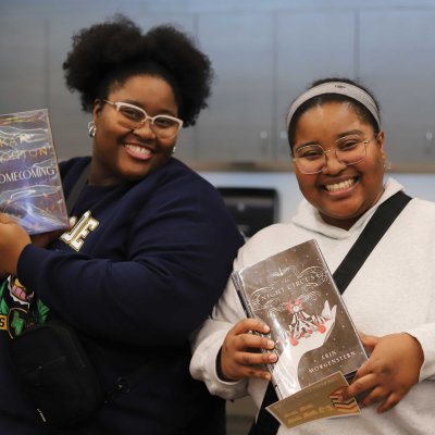Two women holding library books and smiling at camera.