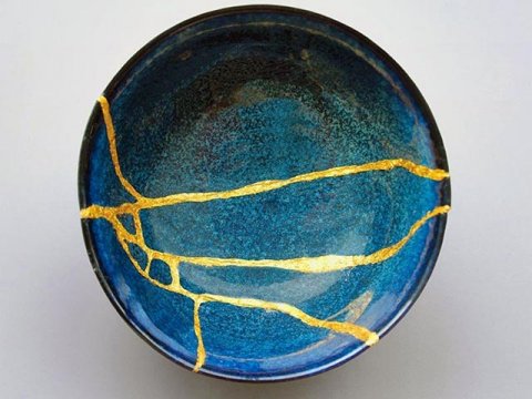 an aqua-blue bowl repaired in the kintsugi style with pieces reattached with gold, leaving it striped with gold veins