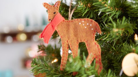 hand stitched brown deer with red scarf hanging from a green christmas tree