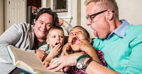 family reading and acting silly while holding book on a sofa