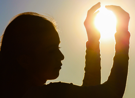 a girl with cupped hands in the air and the sun shining through them, as if holding the sun