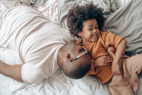 sleeping dad and smiling child on white sheets