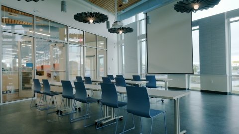 Meeting room at the Almonte Library with a projector, projection screen, and rows of tables and chairs