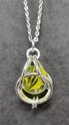 Cats eye Marble trapped in metal rings, hanging from a necklace chain.