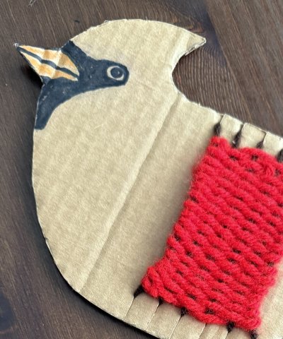 A cardboard loom shaped like a redbird, woven with red yarn