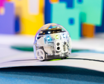 A tiny spherical Ozobot moves along a black line with colorful paper behind it.