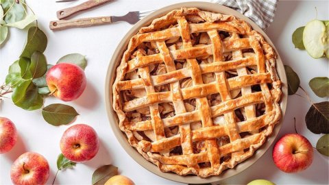 Baked apple pie with a golden crust and several red apples