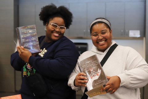 Two women holding library books and smiling at camera.