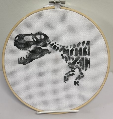 Cross-stitched t-rex skeleton in black thread on white canvas.