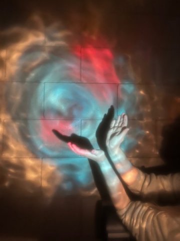 Colored light projected on a wall with a person's hands casting a shadow.