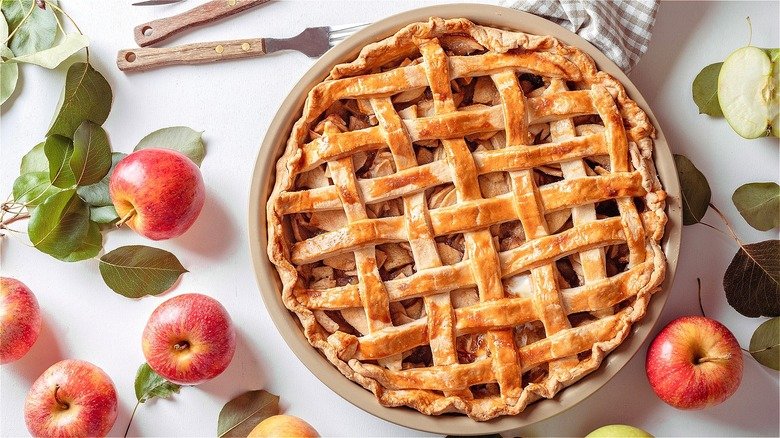 Baked apple pie with a golden crust and several red apples
