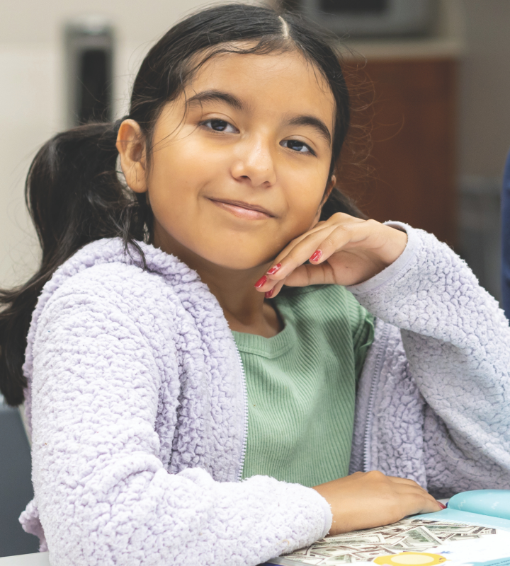 Young girl smiling at camera with a book on a table.