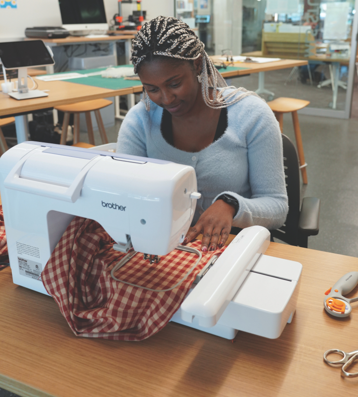 Woman sitting at an embroidery machine working on a project with red and white checkered fabric.