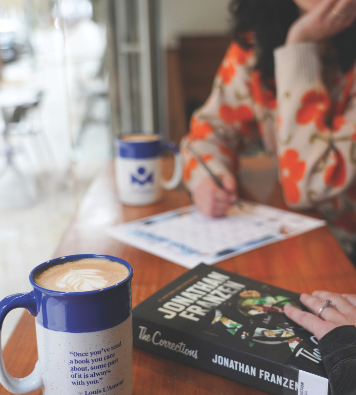Coffee mug and book on table and a person holding a pen near a piece of paper.