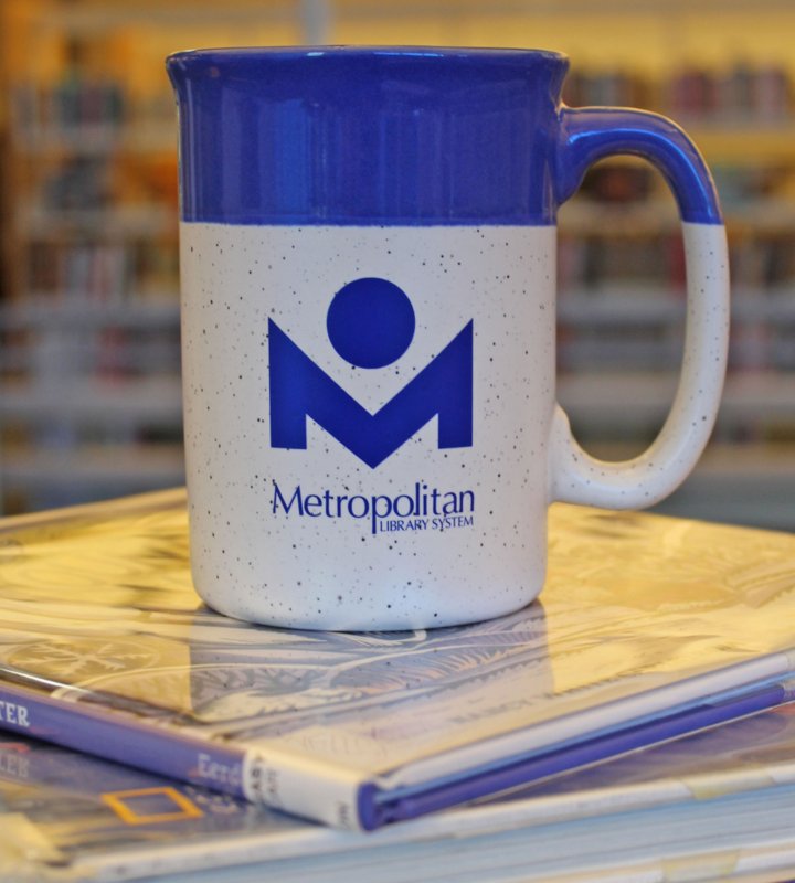 Metro Library branded coffee cup on a stack of books.