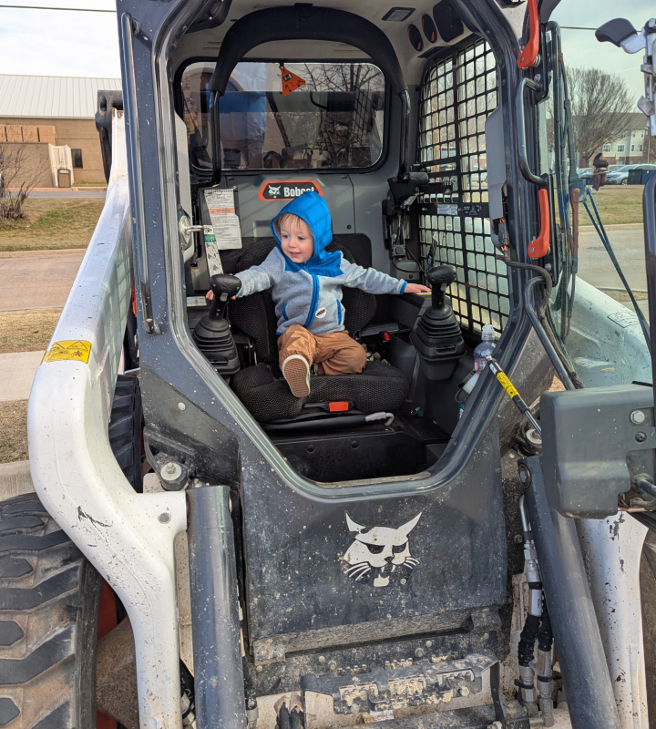 Child wearing a blue hoodie sitting in the operator of a Bobcat skid steer loader.